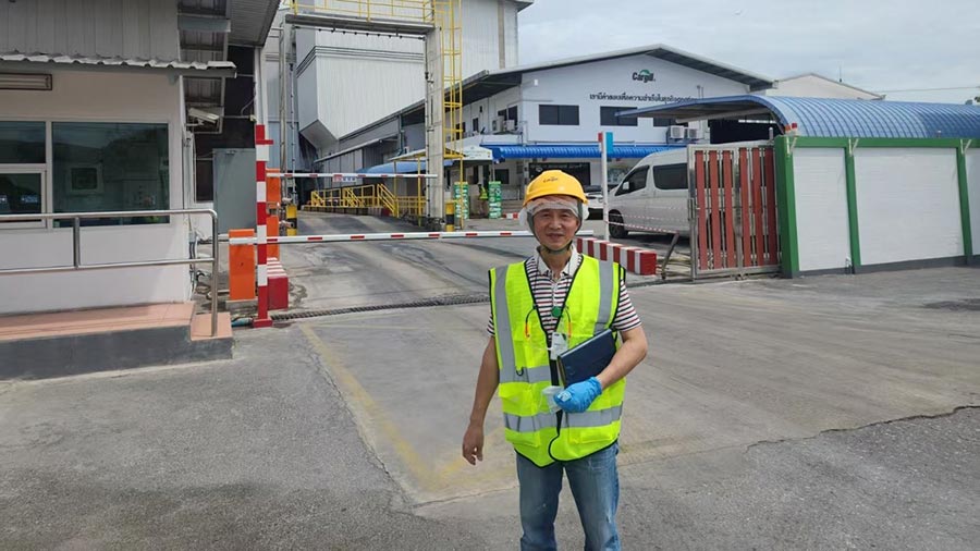 A man wearing a yellow hard hat and yellow safety vest stands outside an operations facility. 